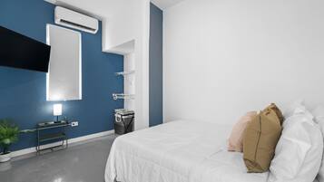 A modern hotel room with a large bed, a bedside table with a lamp, a wall-mounted air conditioner, and a small plant.