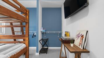 A room with a bunk bed, a TV mounted on the wall, a small table with a plant, and a poster on the wall.