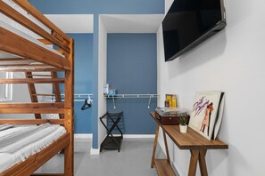 A room with a bunk bed, a TV mounted on the wall, a small table with a plant, and a poster on the wall. - Otium Rentals Perfect Family Getaway Place (San Juan)