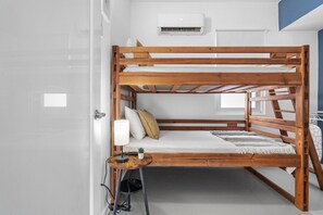 Un lit superposé avec une petite table et une lampe, un climatiseur fixé au mur et une fenêtre avec des stores.