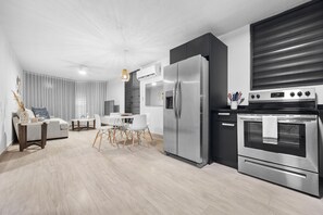 A modern kitchen with a stainless steel refrigerator, oven, and a dining area with a white table and chairs. - Otium Rentals Vacation Getaway at Casa Elena (San Juan)