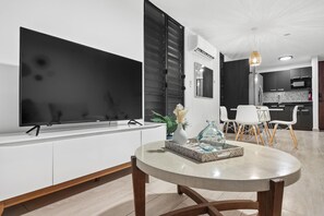 A modern living room with a flat-screen TV, a round dining table, and a kitchen area in the background. - Otium Rentals Vacation Getaway at Casa Elena (San Juan)
