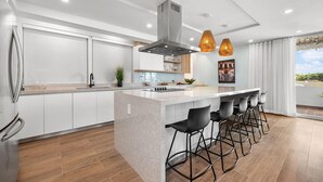 A modern kitchen with a central island, bar stools, and pendant lighting. - Otium Rentals Vacation Rental at Casa Elena (San Juan)