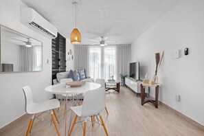 Una sala de estar moderna con comedor, muebles blancos, un ventilador de techo y un televisor.