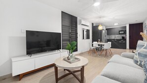 Egy modern nappali, melyben egy síkképernyős televízió, egy kerek dohányasztal és egy szürke színű kanapé található.