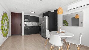 Une cuisine moderne avec des meubles de couleur sombre, un réfrigérateur en acier inoxydable et une table à manger blanche avec des chaises.