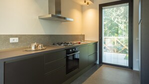 A modern kitchen with a gas stove, oven, and a built-in range hood. There is a window with blinds and a door leading to an outdoor area. - Onda 8 Emma Villas With 4 Bedrooms and 4 5 Bathrooms (Misano Adriatico)