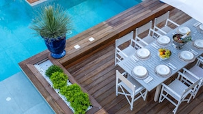 Een houten terras met een zwembad, een gedekte eettafel voor zes personen en een potplant.