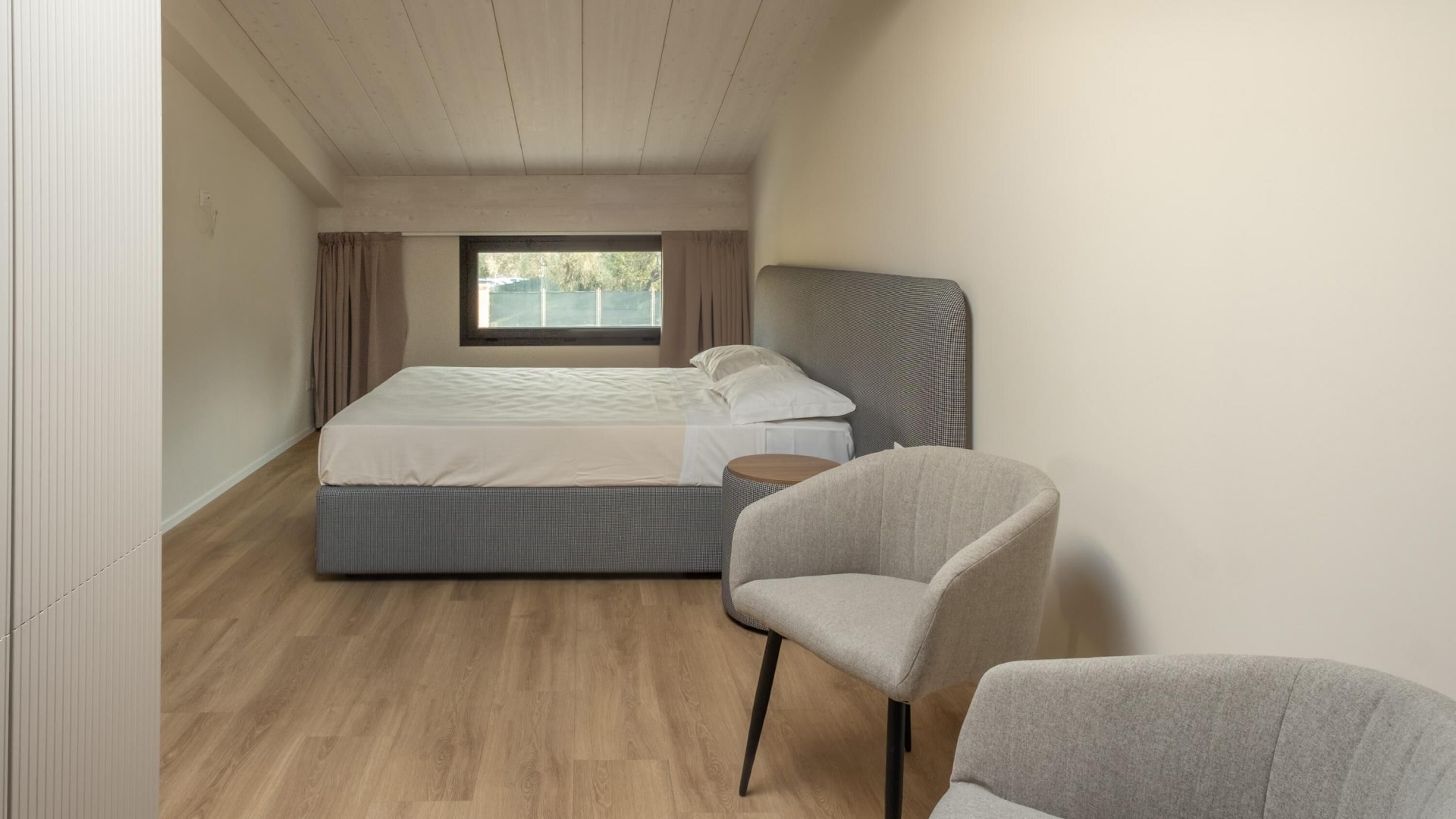 A bedroom with a bed, a chair, and a window.