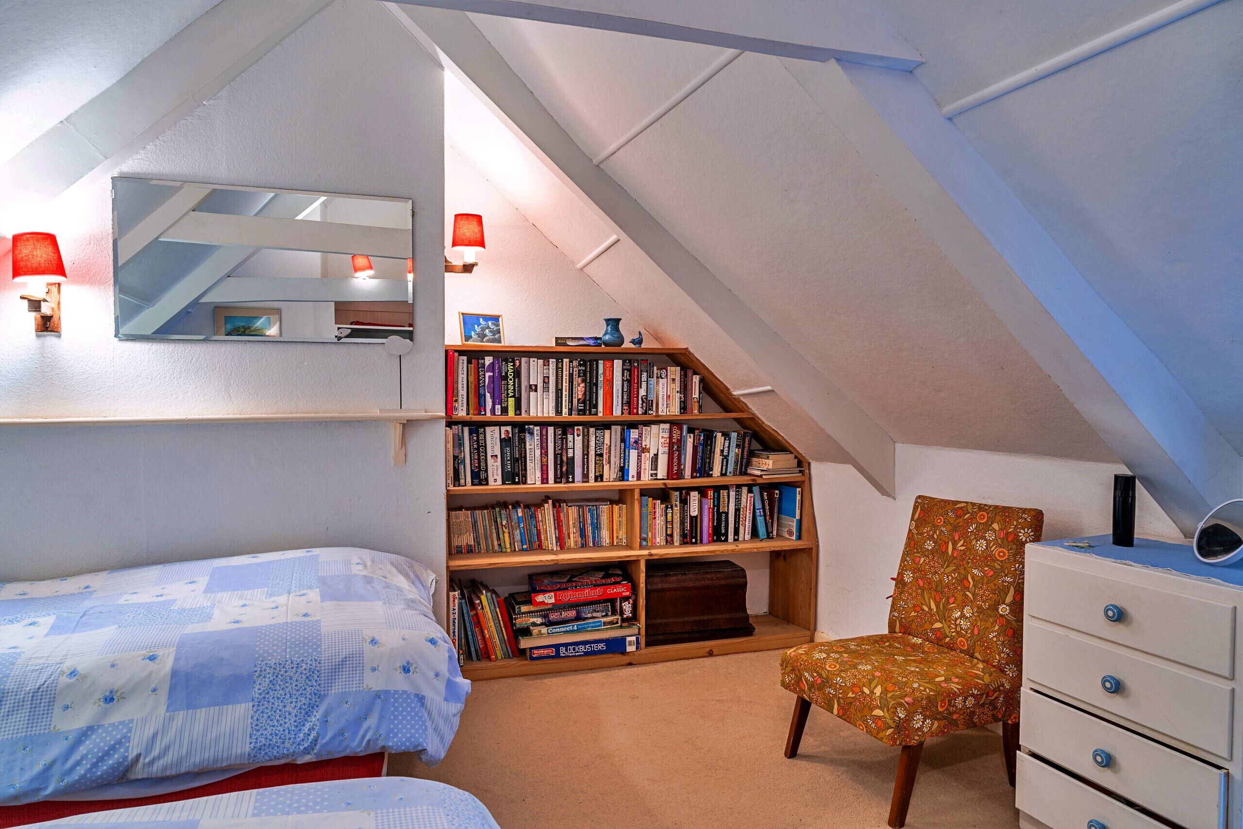 A bedroom with a sloped ceiling, a bookshelf, a chair, and a bed.