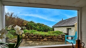 A window with a view of a garden, a stone wall, and a blue chair. - Lewcott (Sennen)