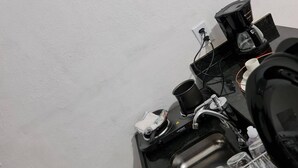 Keittiöalueella on kahvinkeitin, vedenkeitin ja astianpesukone. Työtasolla on valkoinen laatikko.