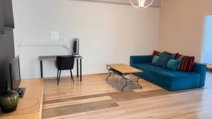 A modern living room with a blue sofa, wooden coffee table, and a black chair. There is a small table with a heater and a TV on a stand. - Bright, comfy, industrial looking (Fällanden)