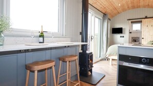 A modern kitchen with a large island, wooden stools, a built-in stove, and a large oven. - Northcott Hut (Bude)