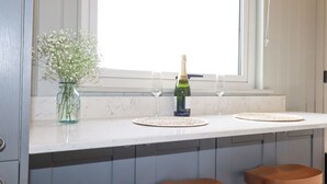 A kitchen counter with a bottle of champagne, two wine glasses, and a vase of flowers. - Northcott Hut (Bude)