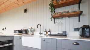 A modern kitchen with grey cabinets, a white countertop, a Bosch coffee machine, and a wooden ceiling. - Northcott Hut (Bude)