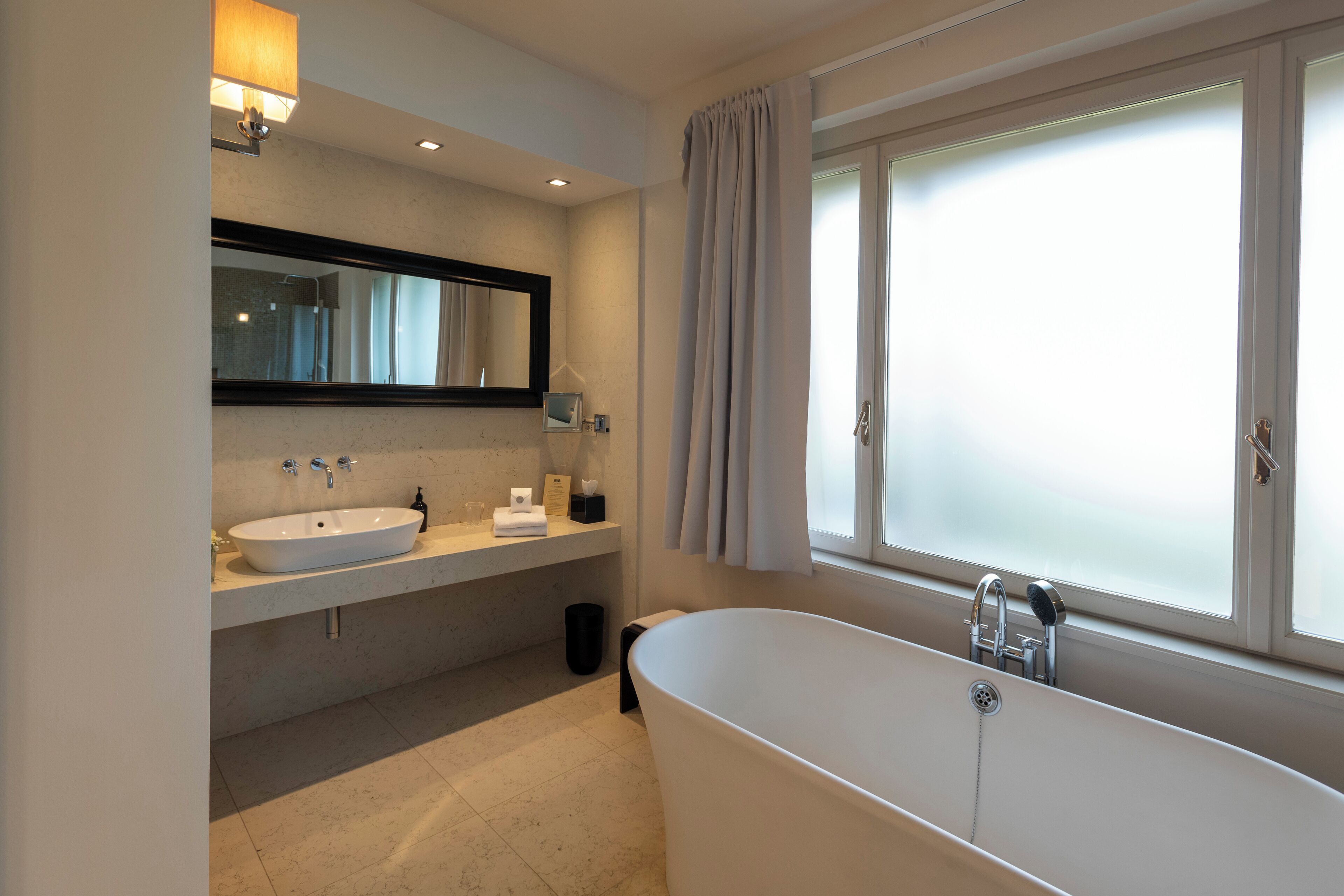 A modern bathroom with a freestanding bathtub, a large mirror, and a vanity with a sink and towel rack.