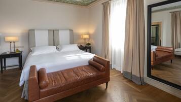 A hotel room with a large bed, two bedside tables with lamps, a large mirror, and a leather sofa.
