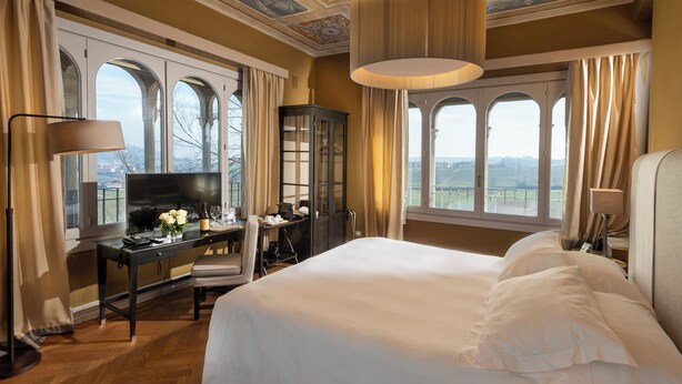 Une chambre spacieuse avec un grand lit, un bureau avec une télévision et une vue sur la campagne grâce à de grandes fenêtres en arc de cercle.