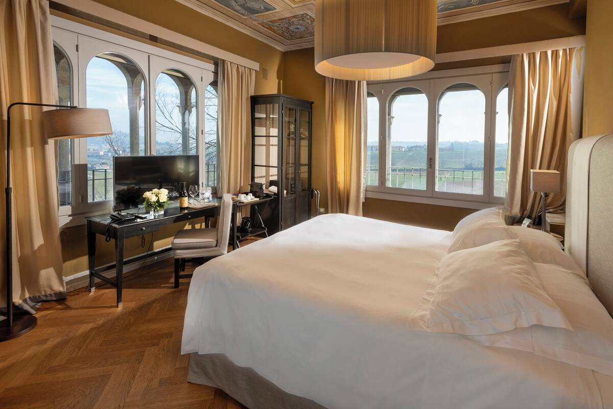 Une chambre spacieuse avec un grand lit, un bureau avec une télévision et une vue sur la campagne grâce à de grandes fenêtres en arc de cercle.