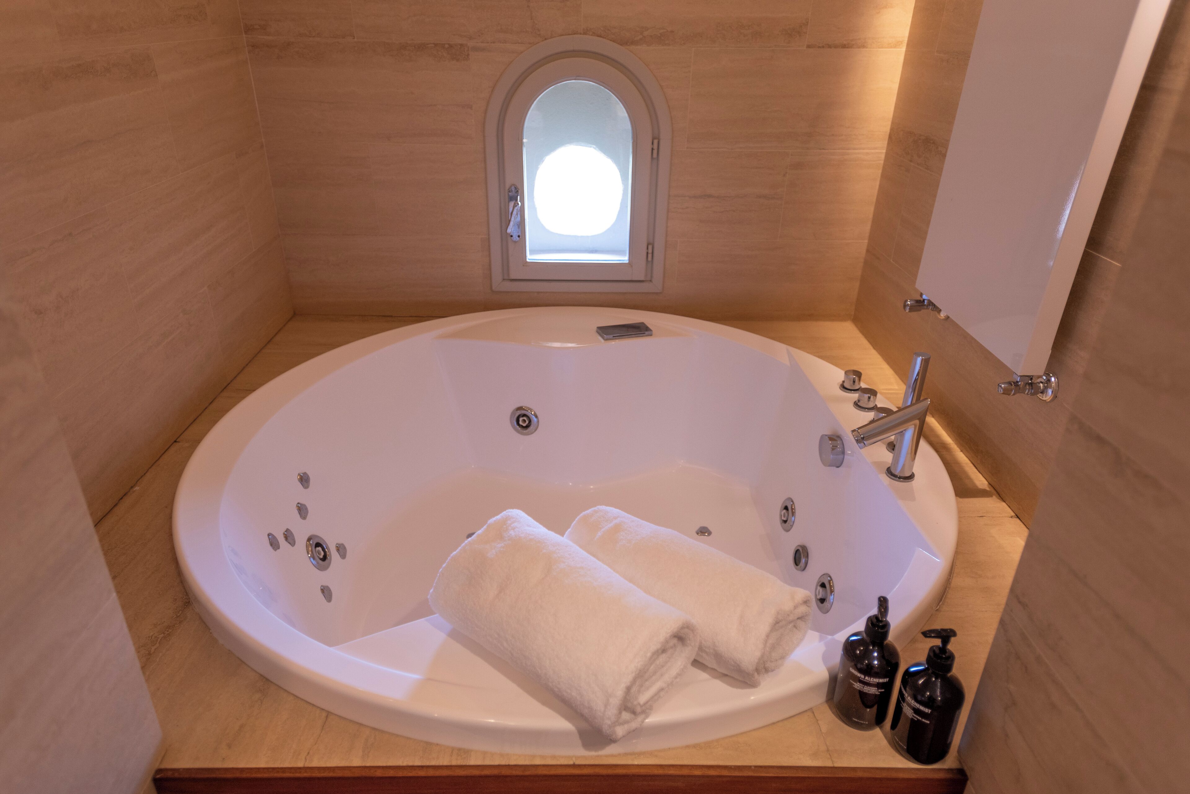 Eine große, ovale Badewanne mit zwei aufgerollten Handtüchern, einem kleinen Fenster darüber und zwei Shampooflaschen seitlich.