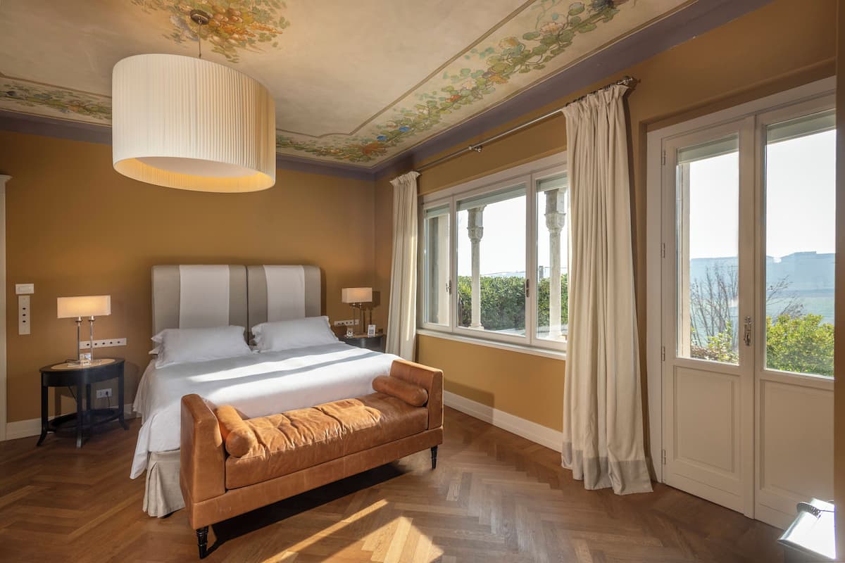 Une chambre à coucher avec un grand lit, un banc, une fenêtre avec des rideaux et un plafond orné de motifs floraux.