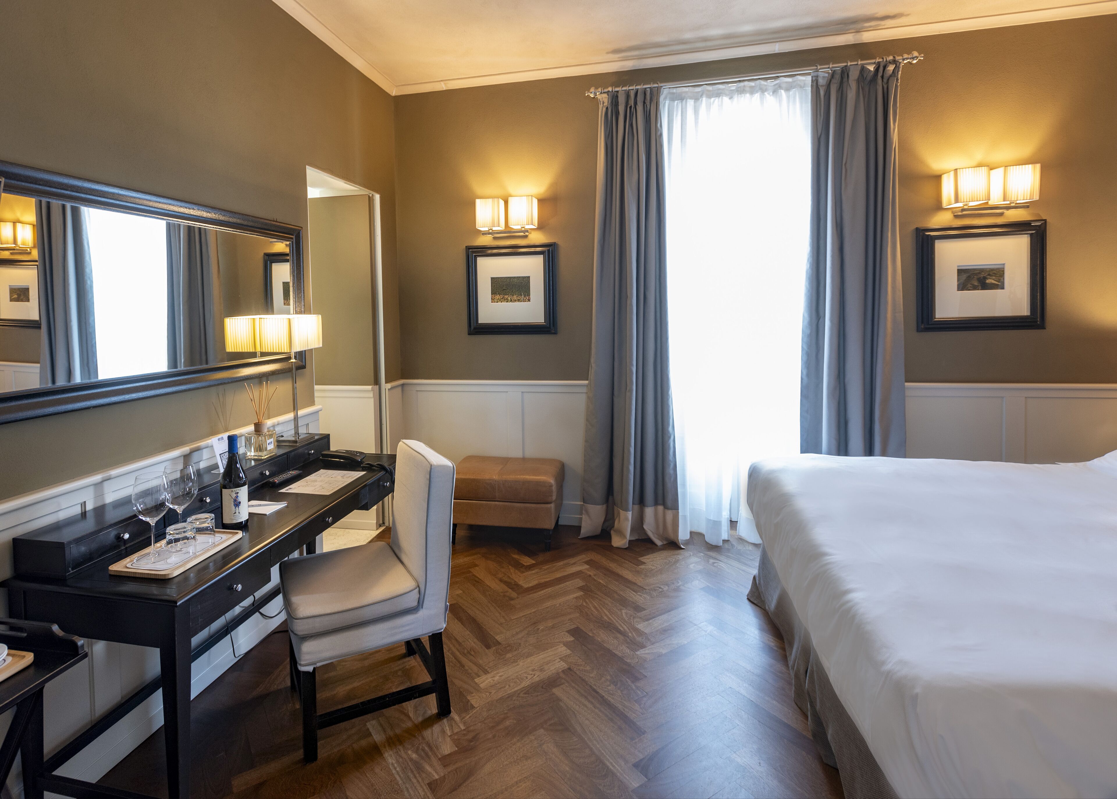 A hotel room with a bed, a desk with a chair, a mirror, and two wall-mounted lamps.
