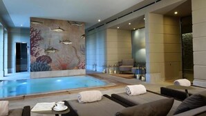 Un espace piscine intérieur moderne, agrémenté d’une fresque murale, de fauteuils confortables et d’une petite table avec une tasse et un menu.