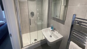 A modern bathroom with a glass-enclosed shower, a white sink, and a mirror. - Arlan House Hotel (Basingstoke)