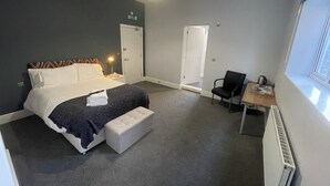 A hotel room with a bed, a desk, a chair, a radiator, and a window. - Arlan House Hotel (Basingstoke)