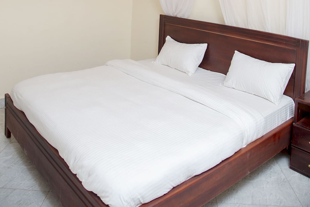 A neatly made bed with white linens, a wooden headboard, and a decorative orange valance.