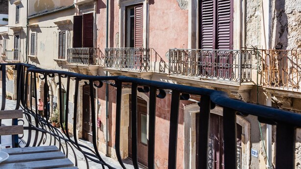 A balcony with a wrought iron railing overlooking a row of buildings with traditional architecture, including balconies and shutters. - La Maison di Ortigia (Syracuse)