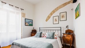 A bedroom with a bed, wooden nightstands, and artwork on the walls. - La Maison di Ortigia (Syracuse)