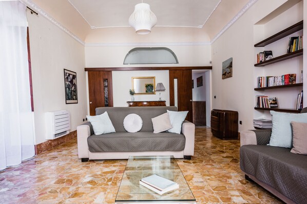A living room with a sofa, a coffee table, a bookshelf, and a decorative mirror. - La Maison di Ortigia (Syracuse)