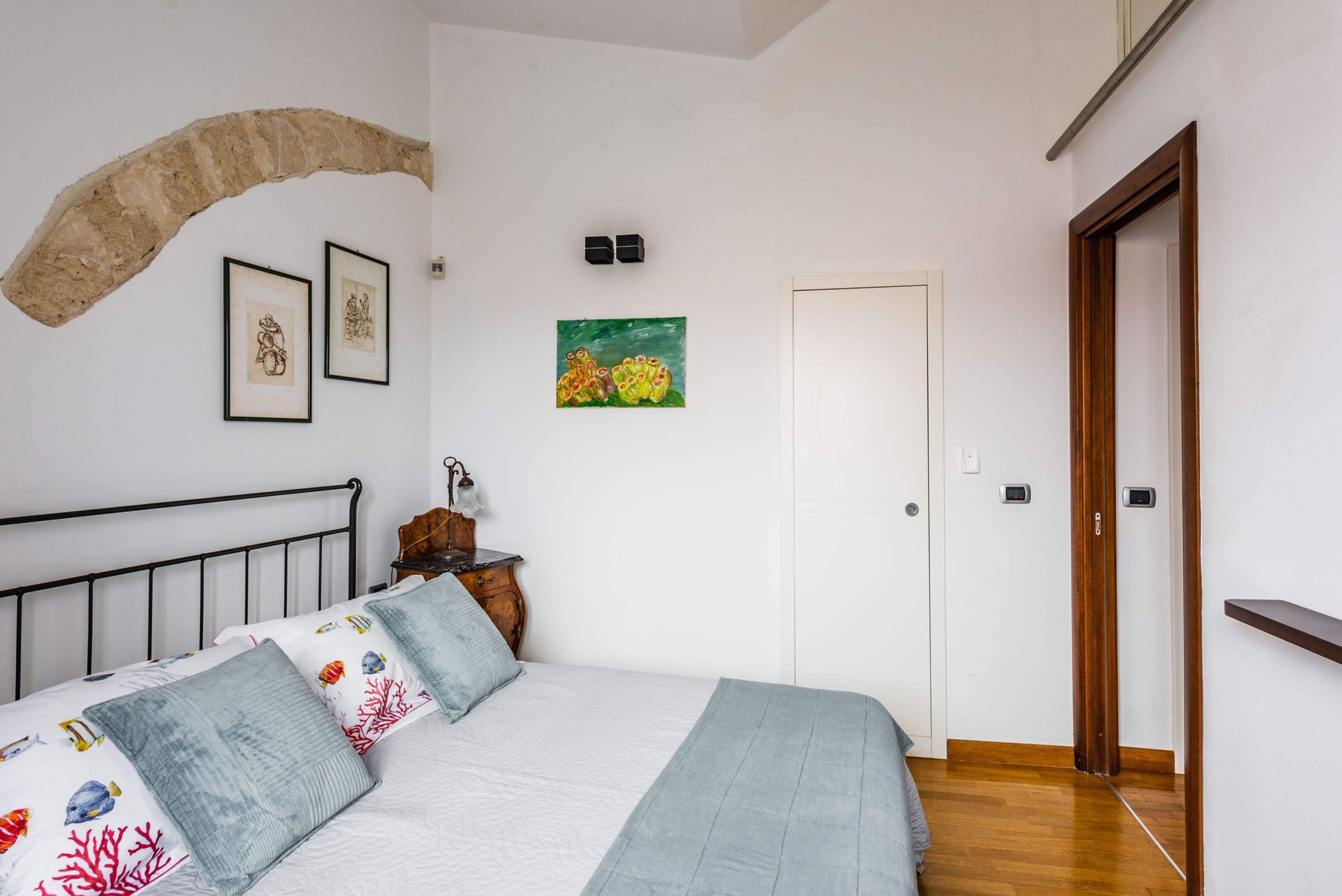 A bedroom with a bed, a wooden headboard, a wall-mounted shelf, a door, and a wall art piece.