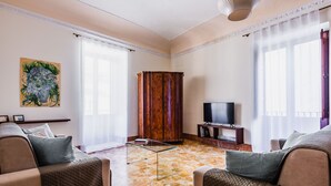 A living room with a sofa set, a glass coffee table, a television, and a decorative painting on the wall. - La Maison di Ortigia (Syracuse)
