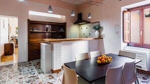 A modern kitchen with a dining area, featuring a stone tile floor, wooden cabinets, and pendant lighting. - La Maison di Ortigia (Syracuse)