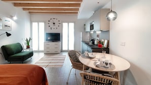 Un salon moderne avec un canapé vert, un coin repas doté d’une table ronde et une cuisine avec des meubles blancs et un luminaire suspendu.