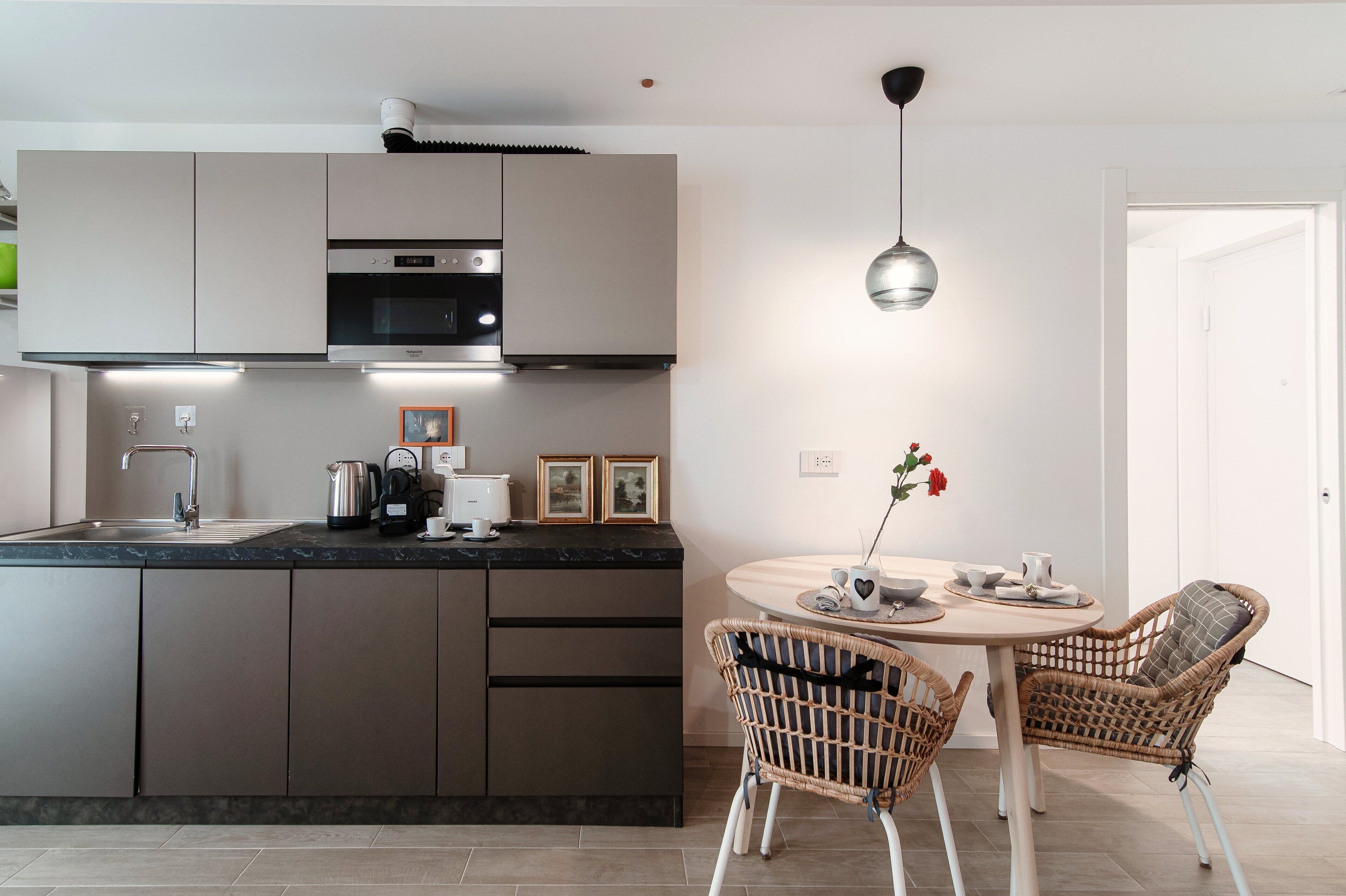 A modern kitchen with built-in appliances, a dining area with wicker chairs, and a pendant light.