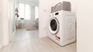 Une buanderie équipée d’un lave-linge à chargement frontal, d’une petite table avec des chaises et d’une porte vitrée donnant accès à une salle de bain.