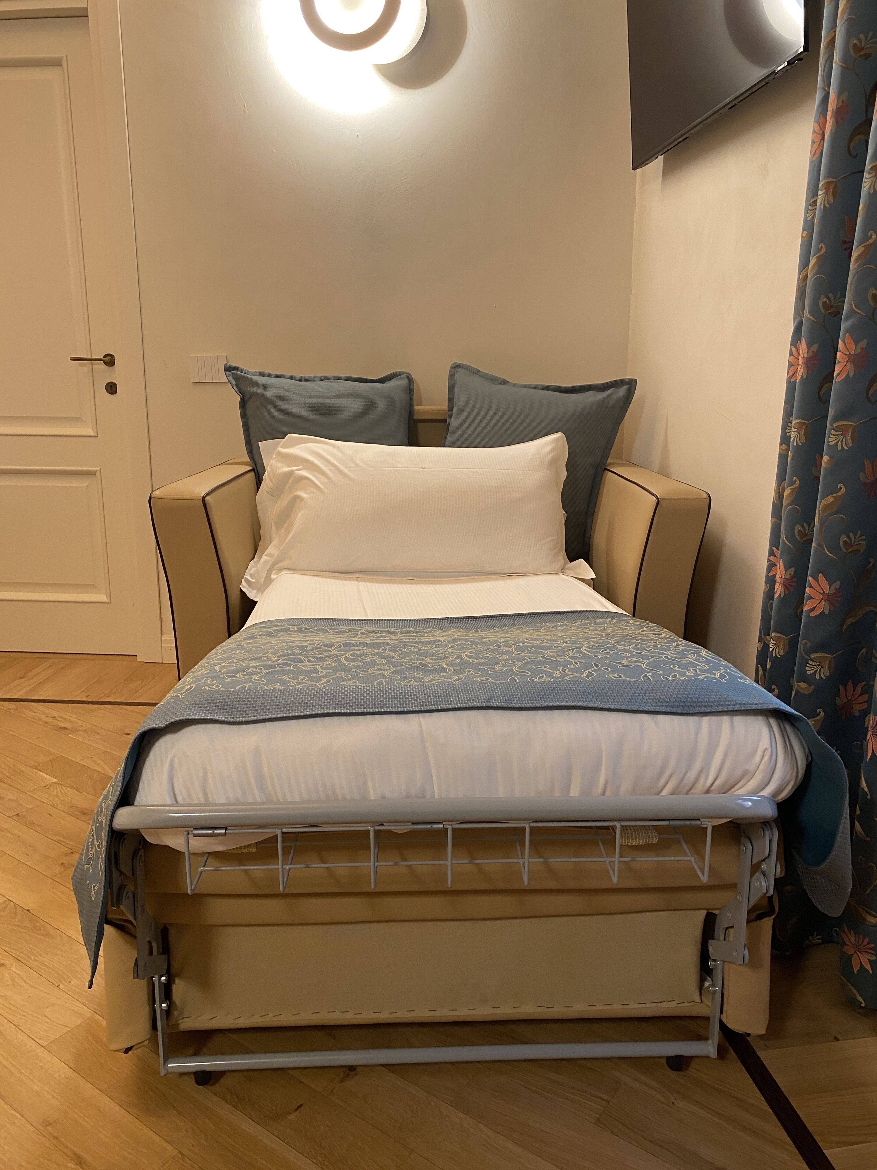 A bed with a metal frame, beige bedding, and a patterned blue blanket.
