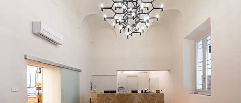 Eine geräumige Lobby mit einer zentral gelegenen Rezeption, einem modernen Chandelier und einem großen Fenster rechts.