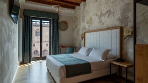 Un dormitorio con una cama grande, vigas de madera en el techo, vistas a través de una ventana y una mesita de noche pequeña.