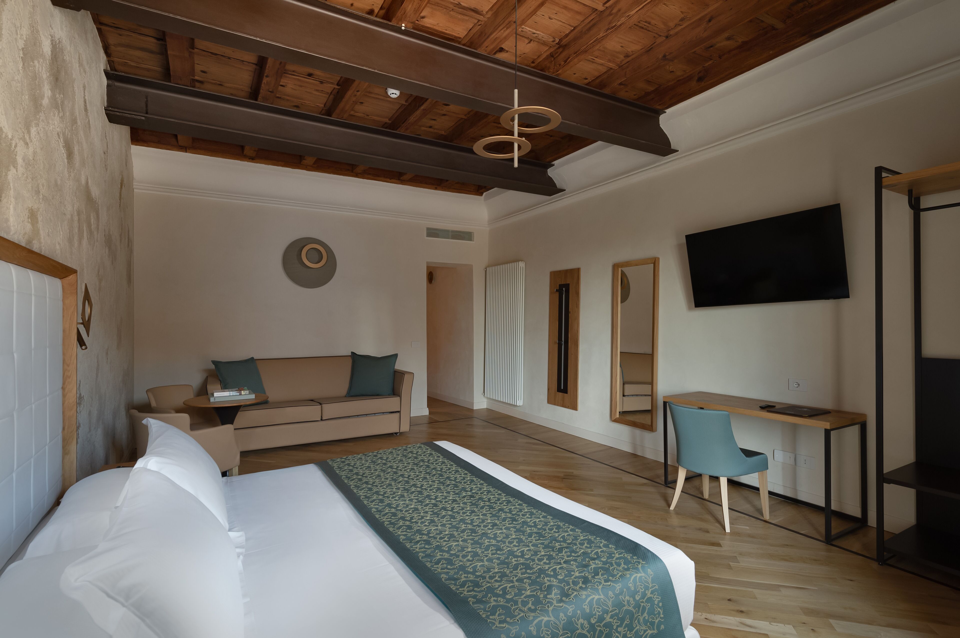 A modern hotel room with a large bed, a desk, a sofa, and a TV.