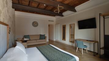 A modern hotel room with a large bed, a desk, a sofa, and a TV.