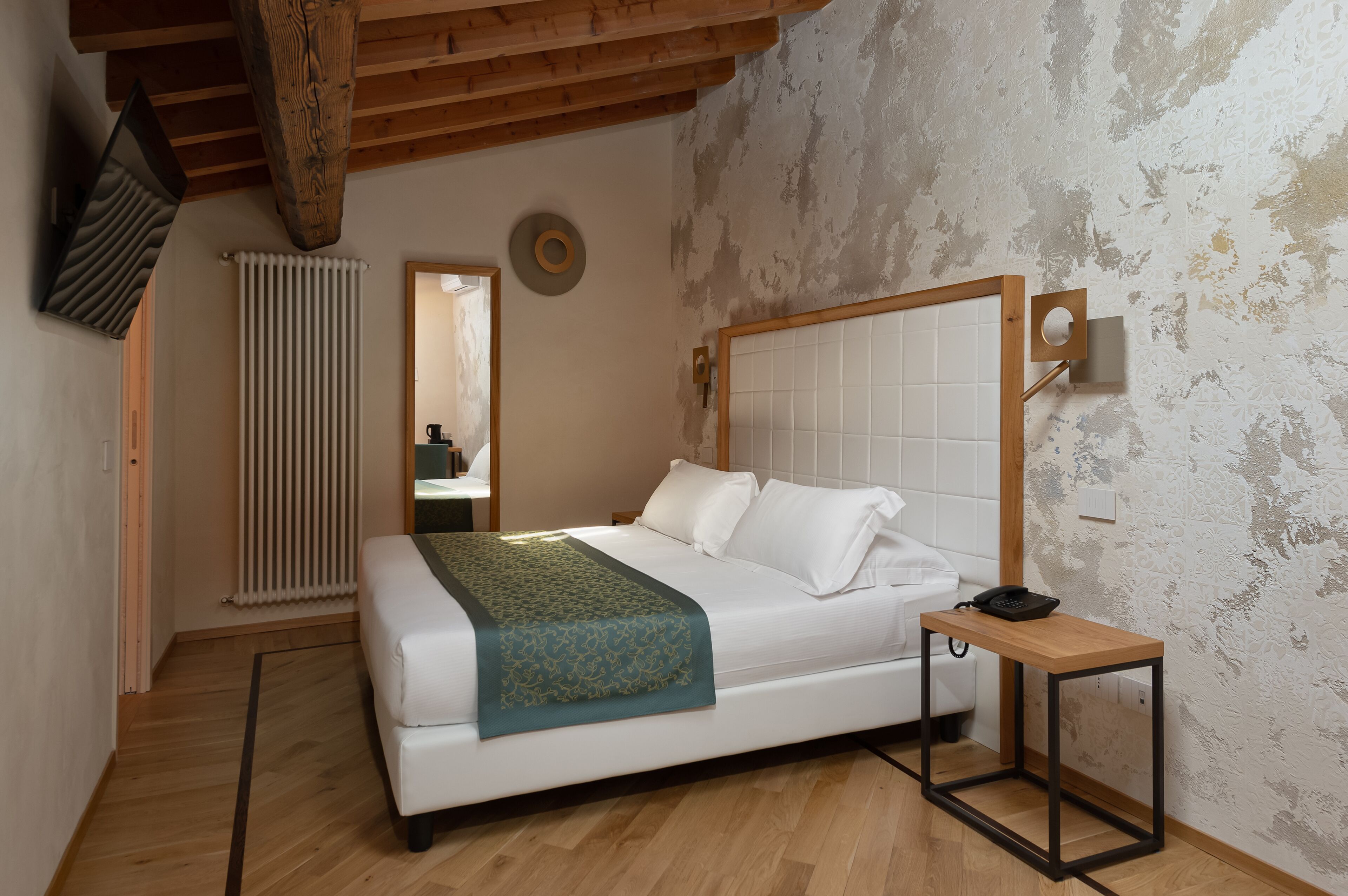 Un dormitorio con techo de madera, una cama con cabecera blanca, una mesita de noche y un radiador.