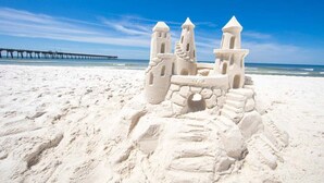 Ein Sandburg am Strand, im Hintergrund ein Steg.