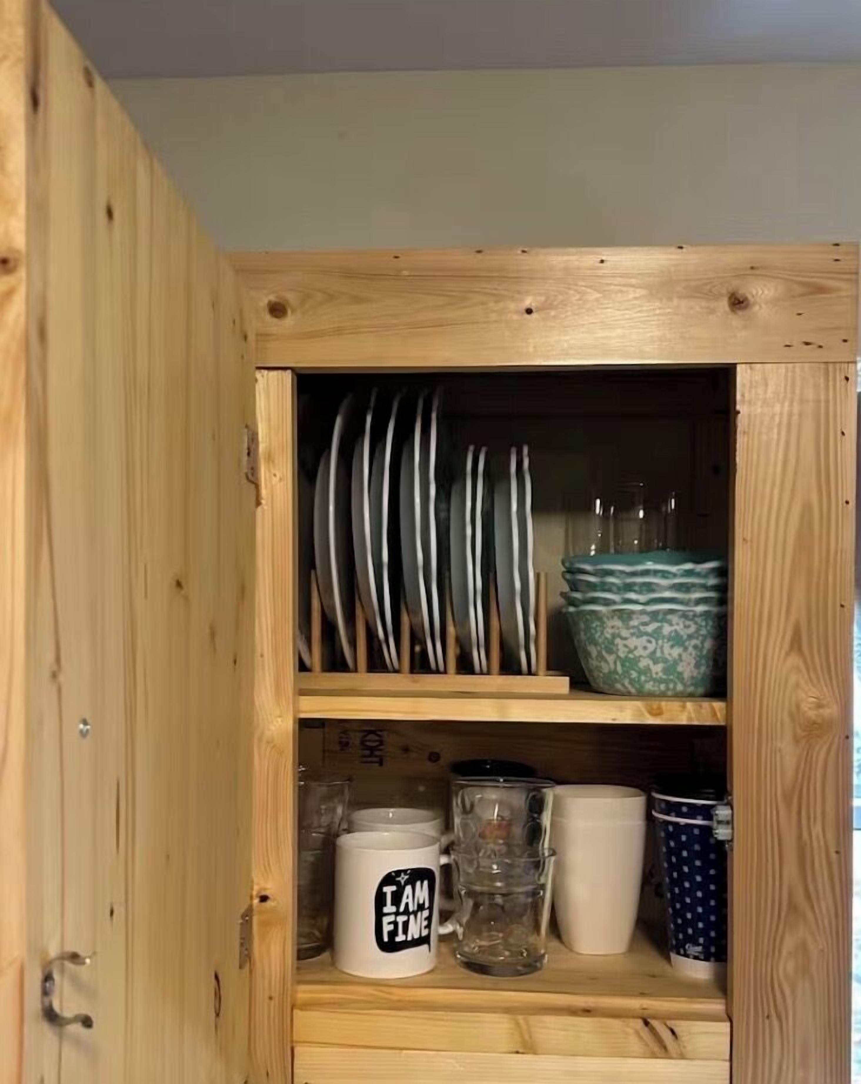 Un meuble en bois doté d’étagères où sont rangées des assiettes, des bols, une tasse et des verres.