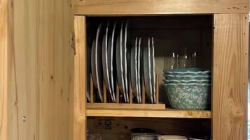 Un meuble en bois doté d’étagères où sont rangées des assiettes, des bols, une tasse et des verres.