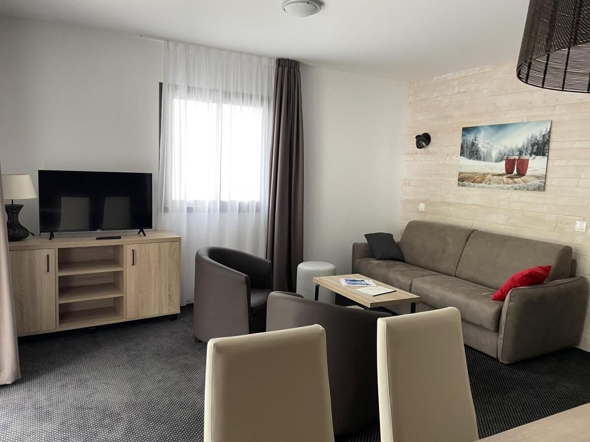 Et moderne hotelværelse med et fladskærms-tv, en sofa, to lænestole, et sofabord og et maleri på væggen.